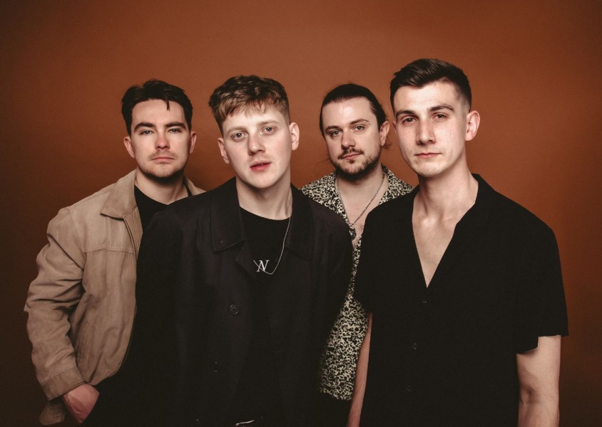 Four men stood in front of a red backdropx